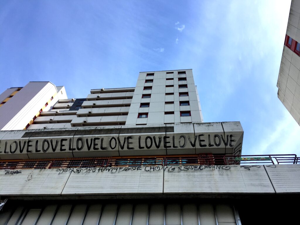 Fassade des Ihme-Zentrum in Hannover vor blauem Himmel. Ein Graffiti Love Love Love ist an der grauen Wand zu lesen.