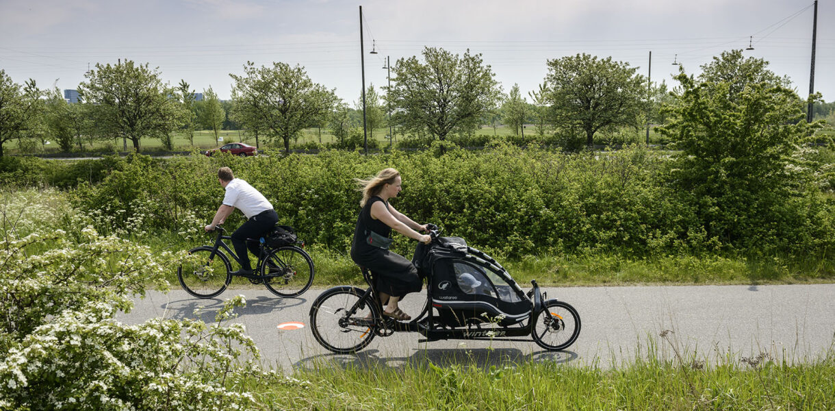 Aufnahme von Fahrrad-Highway in Kopenhagen. Eine Frau und ein Mann fahren durch eine grüne Landschaft.