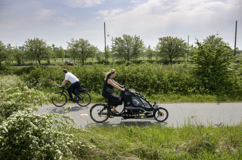 Aufnahme von Fahrrad-Highway in Kopenhagen. Eine Frau und ein Mann fahren durch eine grüne Landschaft.