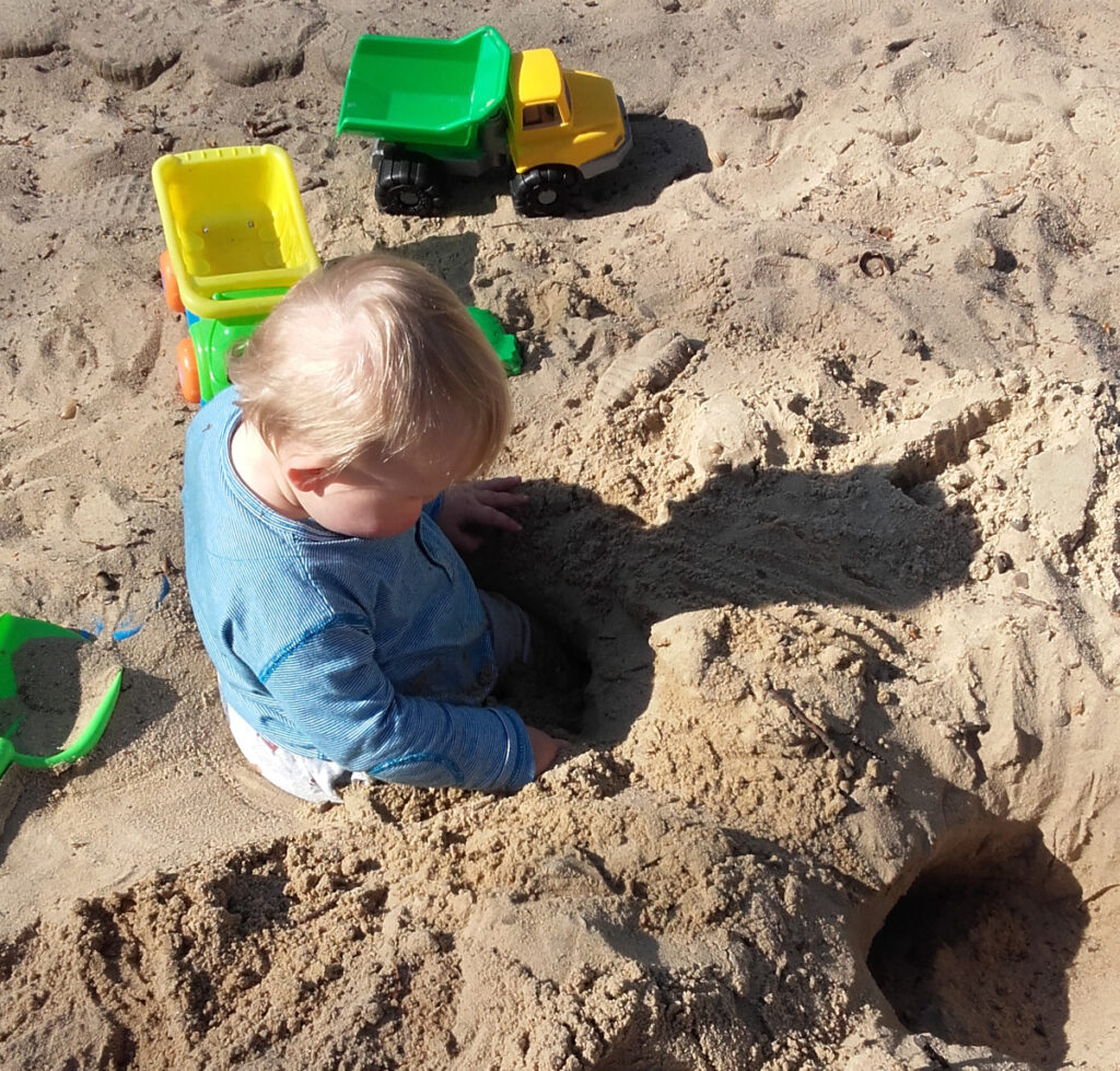 Kleinkind spielt mit verschiedenem Sandspielzeug im Sand.