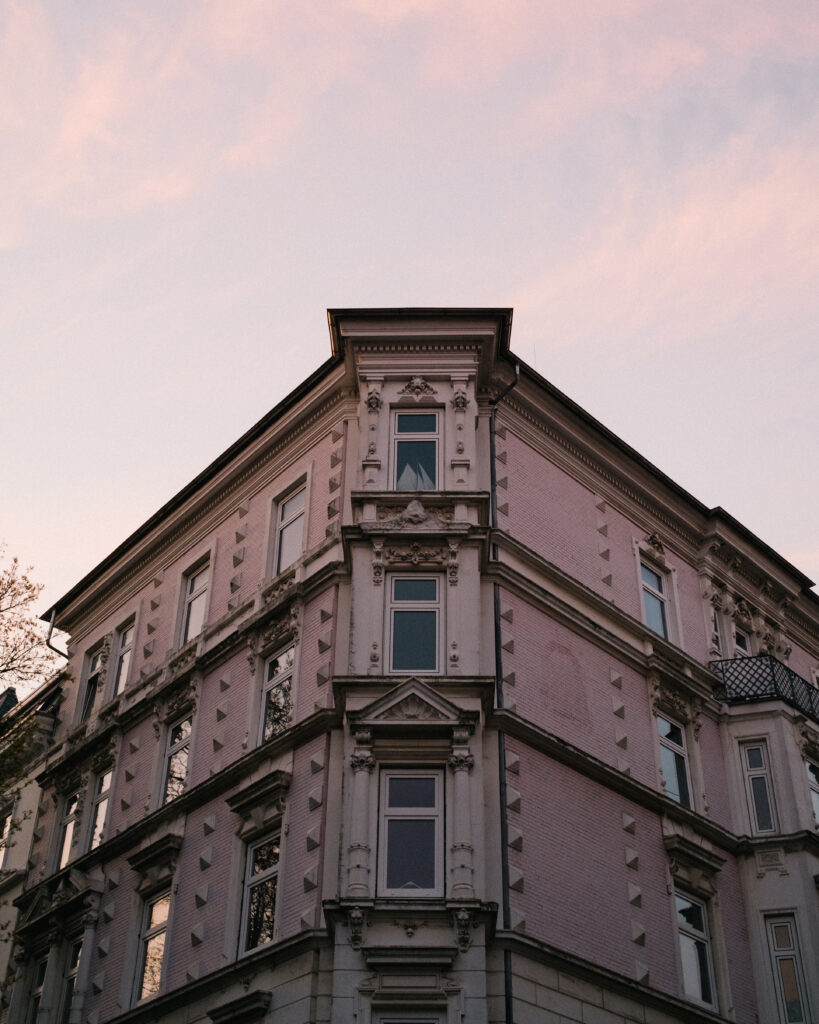 Eckgebäude eines Altbaublocks vor rosafarbenen Sonnenuntergangshimmel