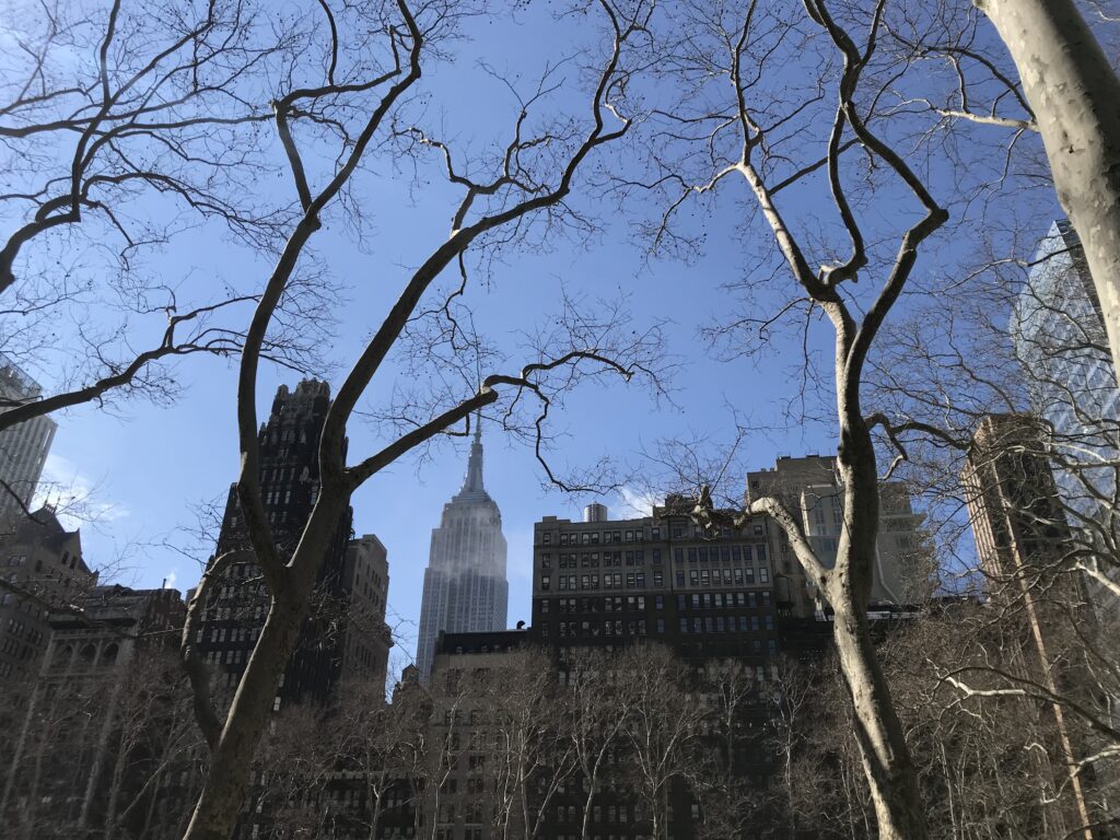 Blick auf das Empire State Buildung durch die kahlen Bäume im Bryant Park New York City