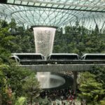 Flughafenhalle in Singapur: Ein Wasserfall fließt von der Glasdecke. In der Flughafenhalle wachsen Bäume.
