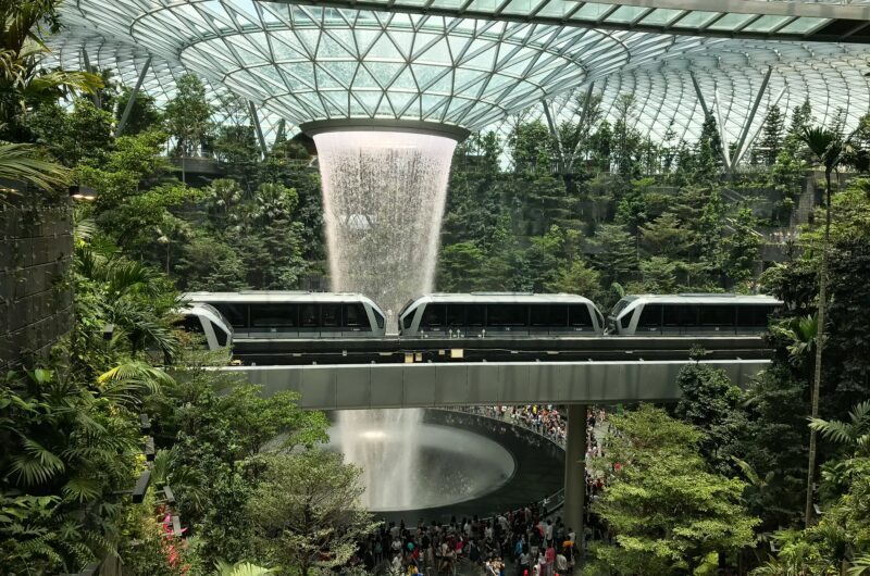 Flughafenhalle in Singapur: Ein Wasserfall fließt von der Glasdecke. In der Flughafenhalle wachsen Bäume.