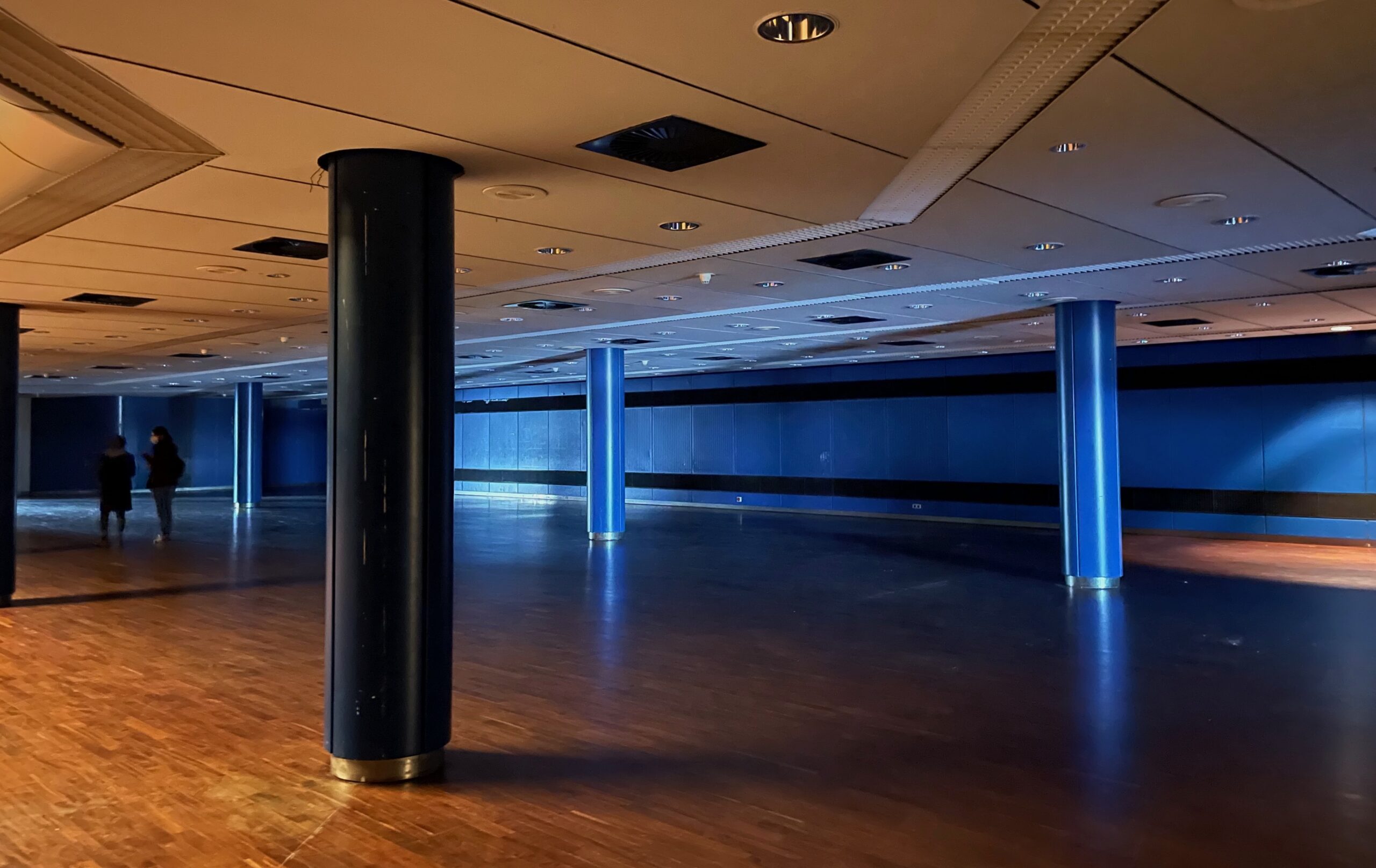 Eine blau erleuchtete leere Halle mit Säulen und Architektur im Stil der 70er Jahre