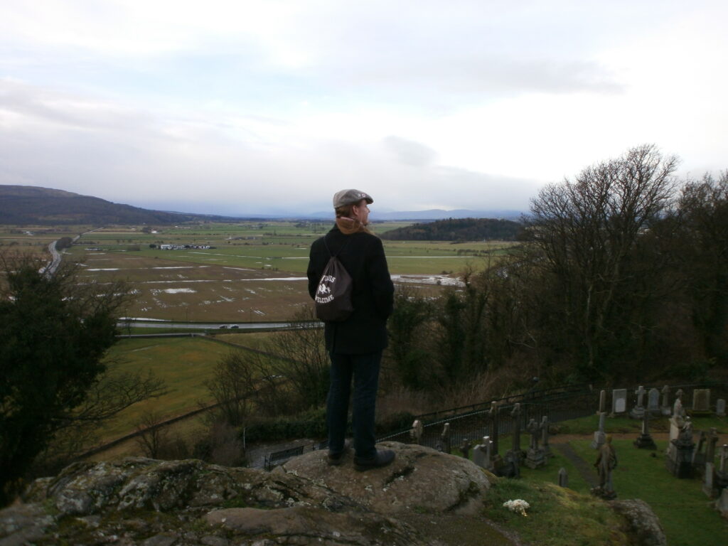 Ein Mann mit Schiebermütze steht vor einer schottischen Landschaft
