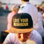 Ein junger Mann trägt ein Cap auf dem steht "Love your neighbours"