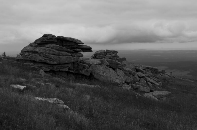 Schwarz-Weiss-Aufnahme von Felsen, die am Abhang eines Berges stehen.