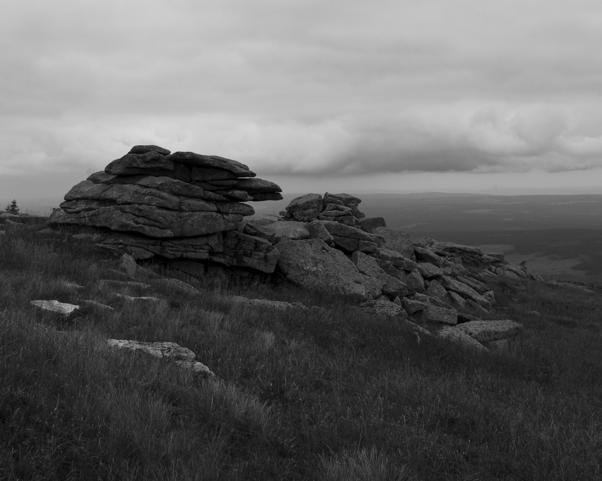 Schwarz-Weiss-Aufnahme von Felsen, die am Abhang eines Berges stehen.