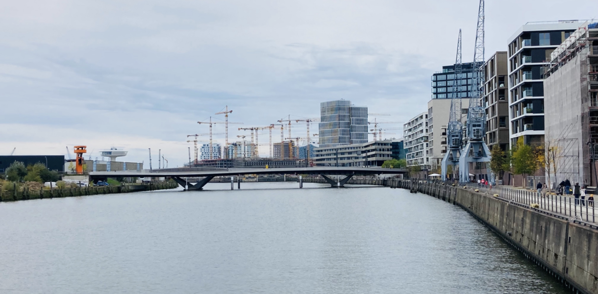 Ansicht von modernen Gebäuden und Kränen in der Hamburger HafenCity. Im Vordergrund ist Wasser
