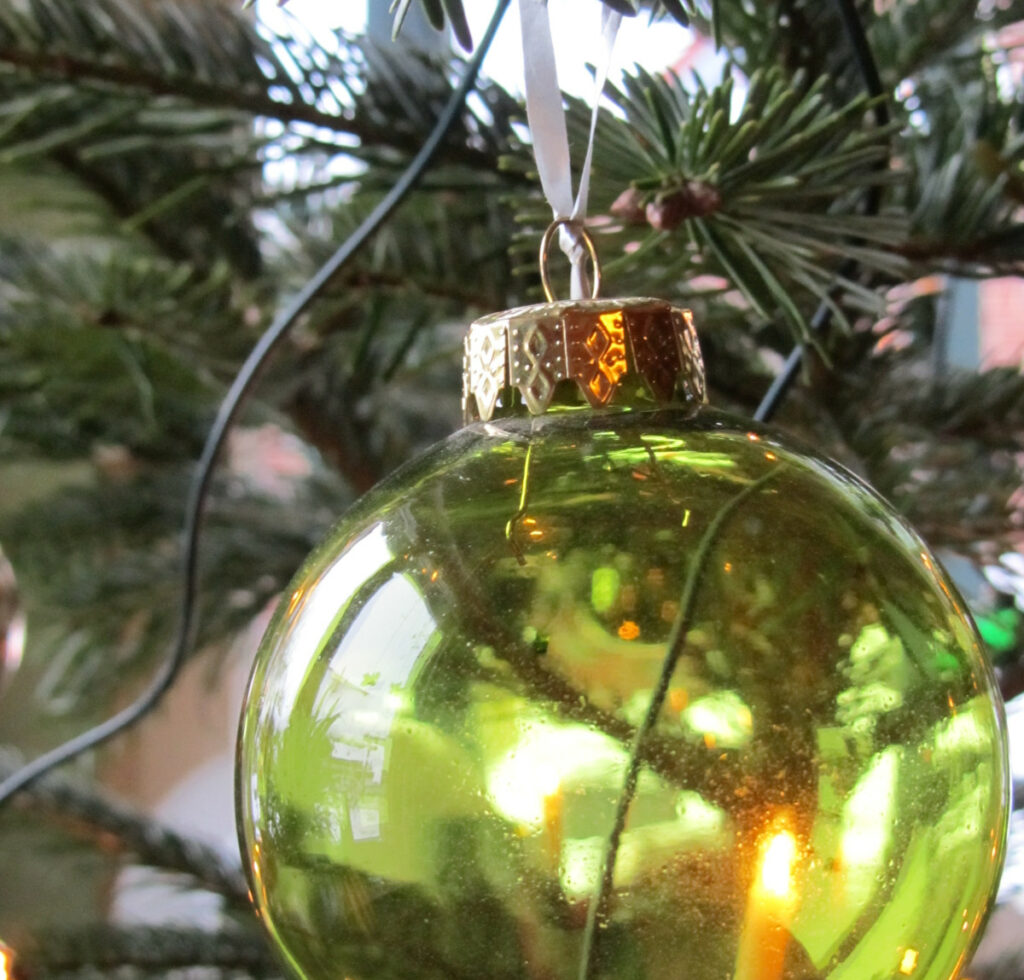 Eine grüne Glaskugel hängt in einem Weihnachtsbaum.