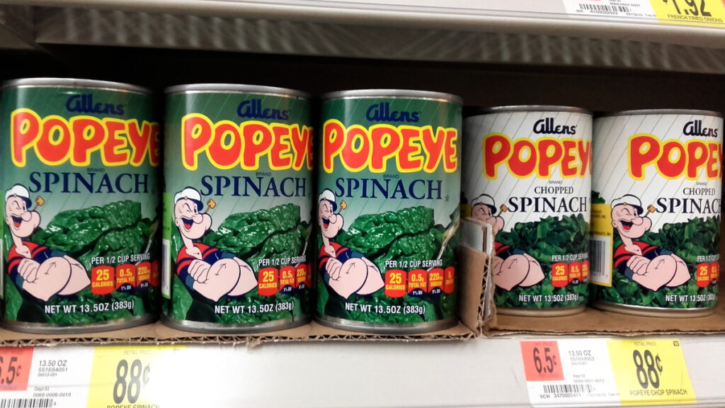 Ein Supermarktregal mit fünf "Popeye" Spinatdosen.