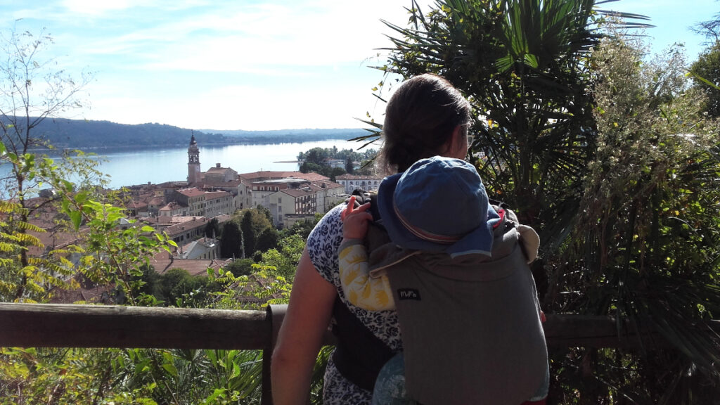Rückansicht auf ein Baby auf dem Rücken einer Frau mit Blick über den Lago Maggiore