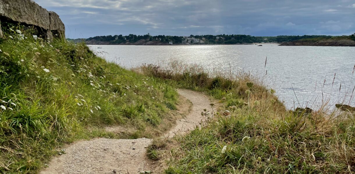 Ein Pfad führt auf einer Klippe entlang mit Blick auf eine Bucht