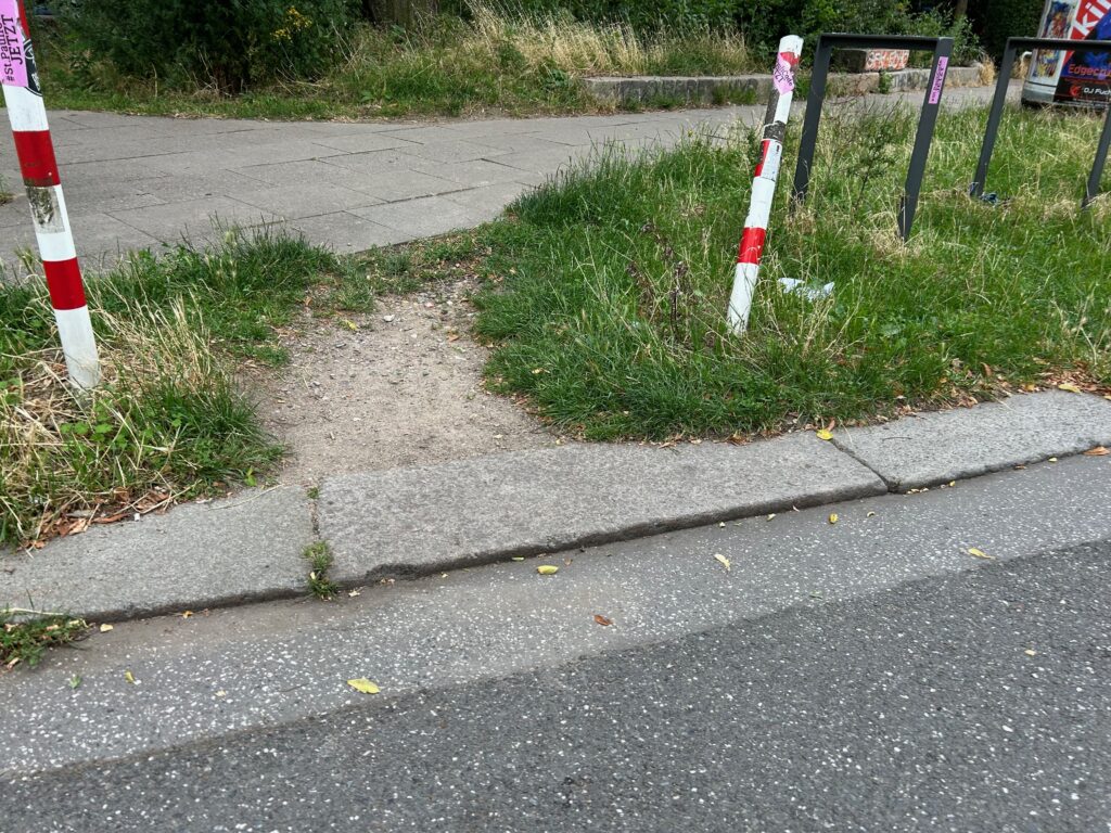 Ein kurzer Trampelpfad durch einen Grünstreifen verbindet die Straße mit dem Bürgersteig