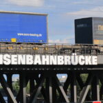 An einer von Containerwagen befahrenen Eisenbahnbrücke im Hamburger Hafen prangt groß das Wort "Eisenbahnbrücke"