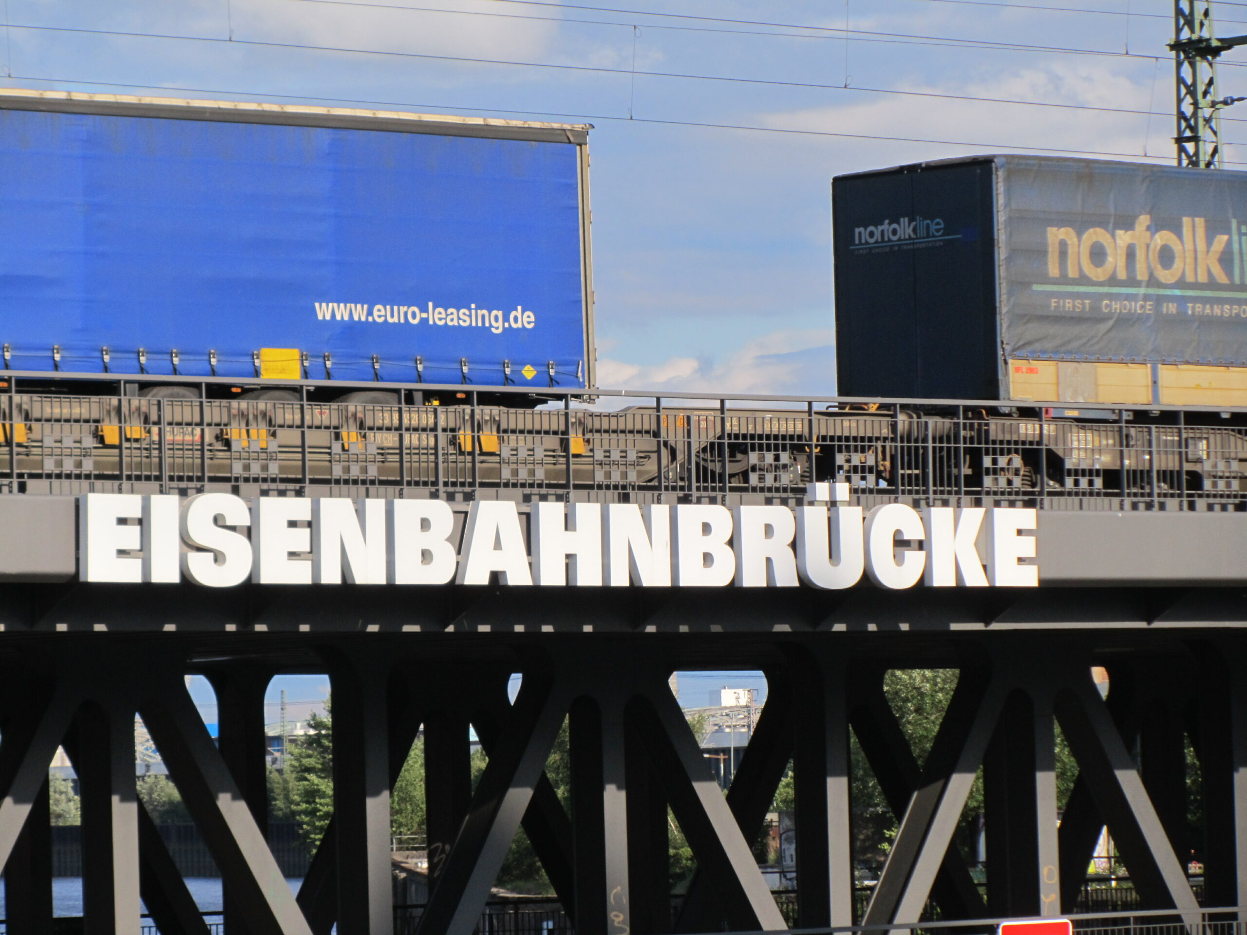 An einer von Containerwagen befahrenen Eisenbahnbrücke im Hamburger Hafen prangt groß das Wort "Eisenbahnbrücke"