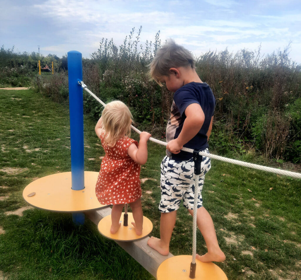 Zwei Kinder, Mädchen und Junge, von hinten auf einem Spielplatz im Grünen